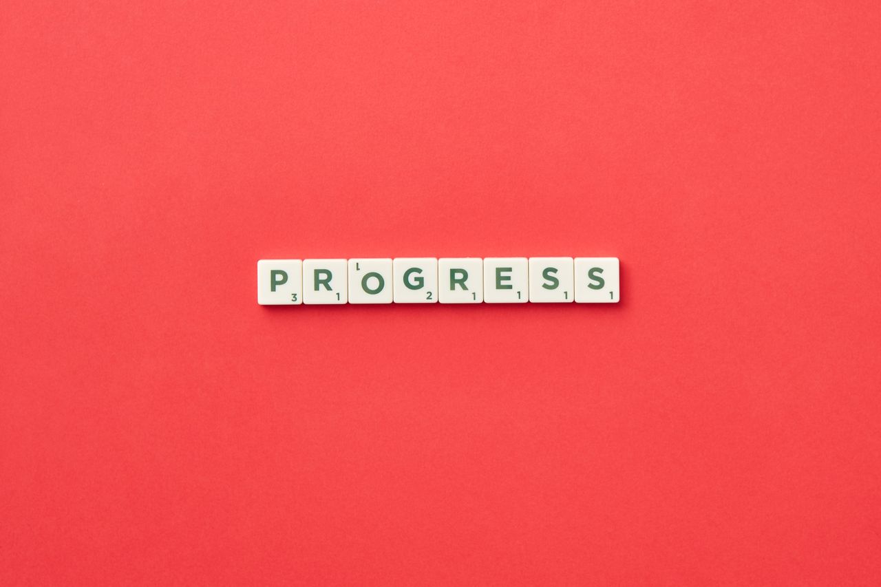 Scrabble tiles spelling Progress on a vibrant red background, symbolizing development.